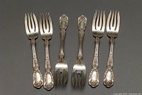 Group of six forks laid handle down showing ornate pattern and monograms
