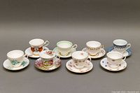 Front view of all eight bone china teacup and saucer sets arranged in two rows showing various floral and decorative patterns.
