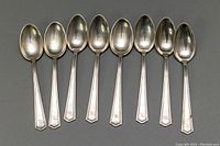 Eight sterling silver coffee spoons displayed side by side, showing front side with monogram 'TRL' on handles.