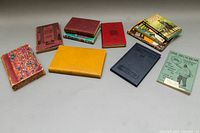 Overall view of collection of 11 vintage and antique books arranged on table, showing mixed bindings and covers with visible age wear.