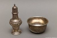 Front and side view of sterling silver salt shaker and bowl on a gray surface, showing overall form and design.