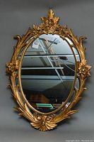 Full view of the oval mirror with the ornate gold frame showing floral and leaf carvings.