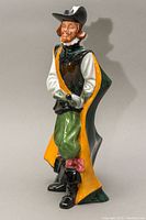 Front and side view of Royal Doulton porcelain figurine depicting a Cavalier in Elizabethan attire with cloak, hat, and sword.