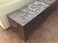 Full view of carved wooden trunk resting on parquet floor beside sofa