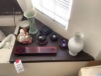 Eight items on dark table: celadon vase, white vase, famille rose bowl, figural teapot and four wooden stands