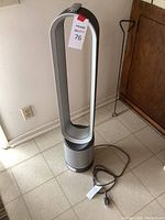 Full view of silver/grey bladeless tower fan standing on tiled floor, power cord visible