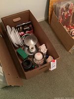 Cardboard lot box showing white plates, decorative metal lidded dish, vases, pink box