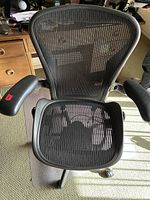 Top-front view of chair seated on clear floor mat showing mesh seat, armrests and mat edges
