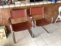 Two brown leather and chrome chairs side by side on tile floor in front of wood panel counter.