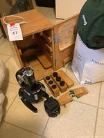 Overall lot display of microscope, wooden lock box, lens caps, power cord, and green bag containing water jugs.