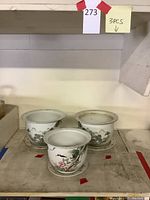 Overall group shot of three ceramic planter pots with saucers on shelf