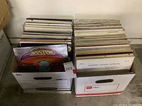 Photo of two boxes filled with vintage vinyl records including a visible Boston album at the front.