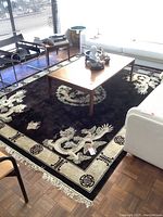 Overall view of rectangular silk rug in living room, showing black field, ivory border, dragon motifs and fringe.