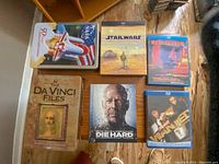 Photo showing the lot's contents including multiple Blu-Ray and DVD cases and a collectible tin featuring NASA's 50th anniversary space shuttle.