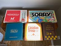 Lot of five board games including Monopoly 80th Anniversary Edition, Sorry, Trivial Pursuit Mastergame Genus Edition, The Art Canadian Trivia, and Chess/Checkers/Playing cards box