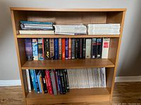 Wooden bookshelf with two shelves filled with books and magazines, showing the overall lot.