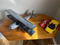 Overall view of the metal biplane and two LEGO Technic cars arranged on a wooden table with natural lighting.