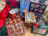 Boxed and loose Christmas ornaments alongside other decorations including a Peanuts-themed hanging ornament, ribbons, and tree skirt.