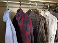 Seven men's shirts hung on hangers on a closet rod showing colors and styles