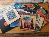 Photo showing a pile of various vinyl records with visible covers including Nat King Cole and others, multiple records stacked loosely with some covers bent or worn.