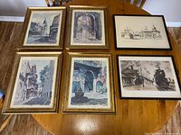 Overview of six framed prints showing architectural scenes and a vintage train imagery on wooden table