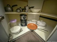 Overview of all kitchen items showing coffee maker, frying pan, kettle, pots, colander, casserole dishes, juice jug and mixing bowl on shelves.