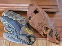 Photo of both vintage baseball gloves placed on a wooden surface showing front and back sides.