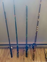 Four fishing rods standing upright against wall, each with attached spinning reel