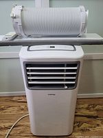 Front view of portable air conditioner with flexible exhaust hose and window vent panel attached