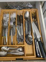 Drawer with organized stainless steel cutlery including forks, knives, spoons and teaspoons in a bamboo utensil tray.