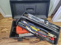 Open black plastic toolbox with various hand tools including pliers, screwdrivers, cutting tools, scissors, and an orange Black & Decker case