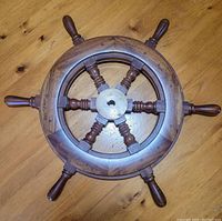 Top view of wooden helm wheel showing circular ring, eight turned wooden handles, and central brass hub