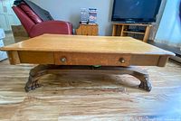 Front view of table showing rectangular top, center drawer with two knobs and carved pedestal base