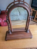 Front view of an oval vintage wooden free standing mirror with turned wooden supports and a rectangular base on a wooden surface.