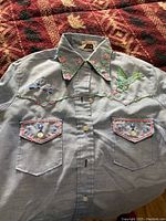 Front view of vintage Wrangler women's shirt with embroidery on chest, collar, and pockets in light blue fabric.