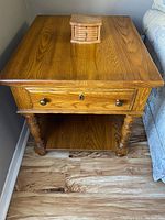 Front view of wooden side table with drawer and small box on top, placed next to couch.