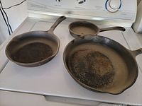 Three cast iron skillets of different sizes displayed on a stove showing wear and cooking residue