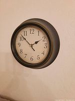 Clock mounted on a beige wall showing time 2:50 and some seconds past 10.
