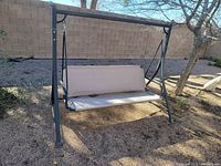 Full view of the metal frame swing showing the structure, beige plastic seat and backrest, and the hanging mechanism with metal springs.