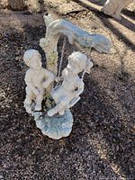 Full view of the statue showing a boy sitting on the base and a girl on a swing hanging from a floral vine-wrapped branch.