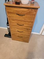 Photo showing wood cabinet with four drawers against a wall and carpet floor.