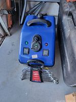Blue electric device with handle, two switches, pressure dial, and indicator lights, with Duralast wrench set in front.