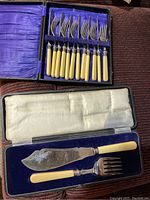 Set of 6 forks and 6 knives with ivory handles in purple satin-lined box, plus cake server and serving fork in separate velvet-lined box with cream satin lid
