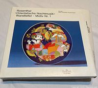 Photo of the closed original white Rosenthal box featuring an image of the decorative plate with colorful abstract figures on a deep blue background