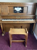 Front view of the oak player piano showing keyboard, roll mechanism window, and matching bench.