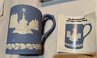 Front view of Wedgwood jasperware mug showing pale blue color, Piccadilly Circus design in white relief, and leaflet about 1971 Christmas mug.