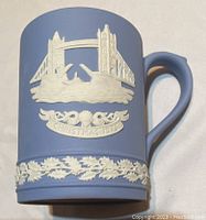 Close up of pale blue jasperware mug showing white relief of London Tower Bridge and inscription 'Christmas 1975' with floral band at bottom.