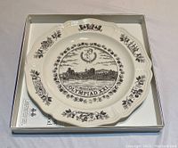 Top view of 10-inch white Wedgwood Olympiad XXI Montreal plate in original box with leaflet visible underneath.