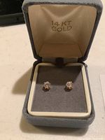 Pair of 14k gold stud earrings with clear stones inside gray velvet jewelry box stamped '14 KT GOLD'.