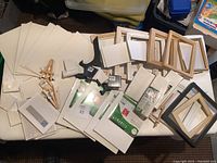 Overview of entire lot showing canvases, wooden and plastic frames, small easels, and display stands all arranged on a table.